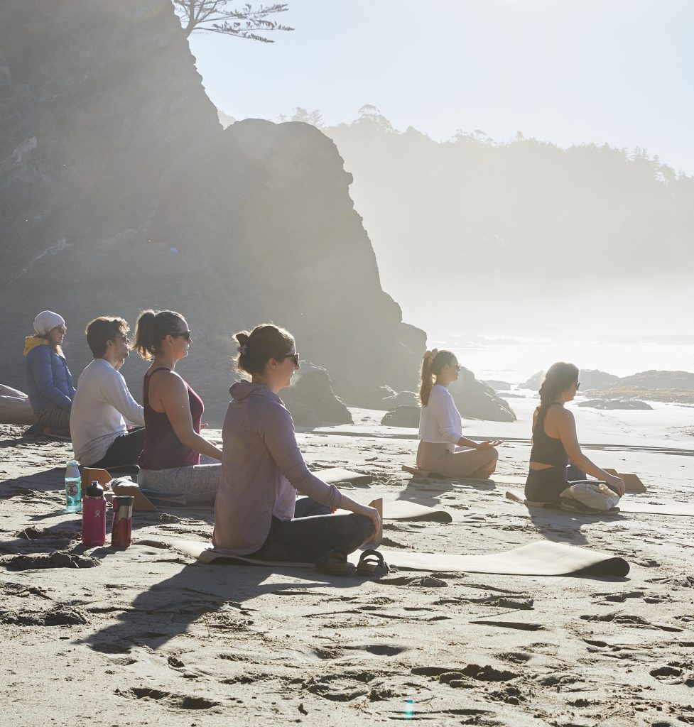 a group of people sitting in meditation pose on the beach