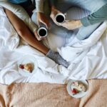 Couple enjoying coffee and fresh pastries in bed with cozy loungewear and white linens at Mar Vista Farm and Cottages.