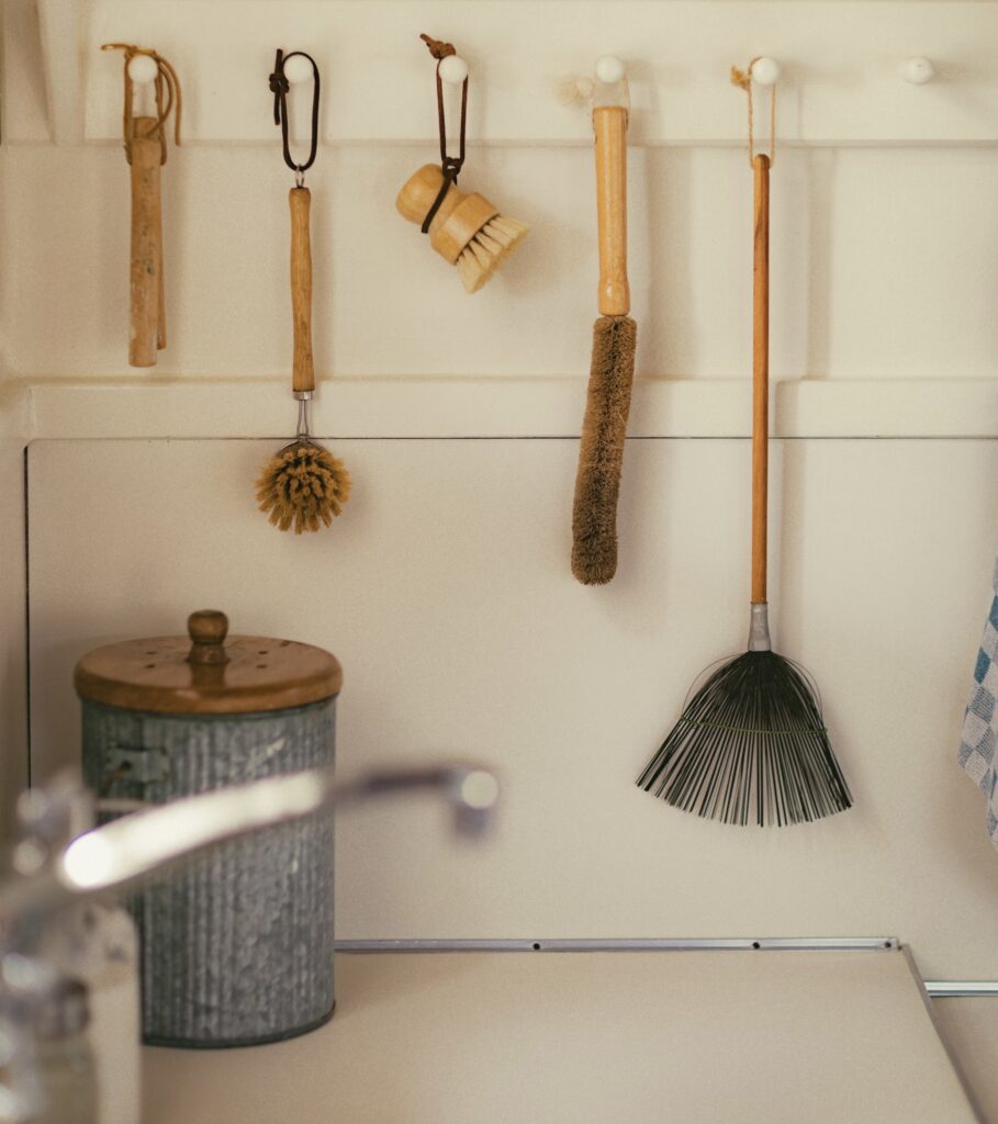Rustic kitchen tools neatly hanging on wooden pegs inside a cozy cottage at Mar Vista Farm and Cottages, featuring natural bristle brushes and a handmade broom.